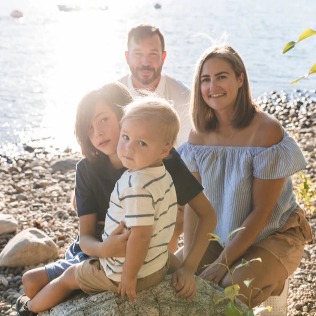 Family of four sitting on a rock by a body of water