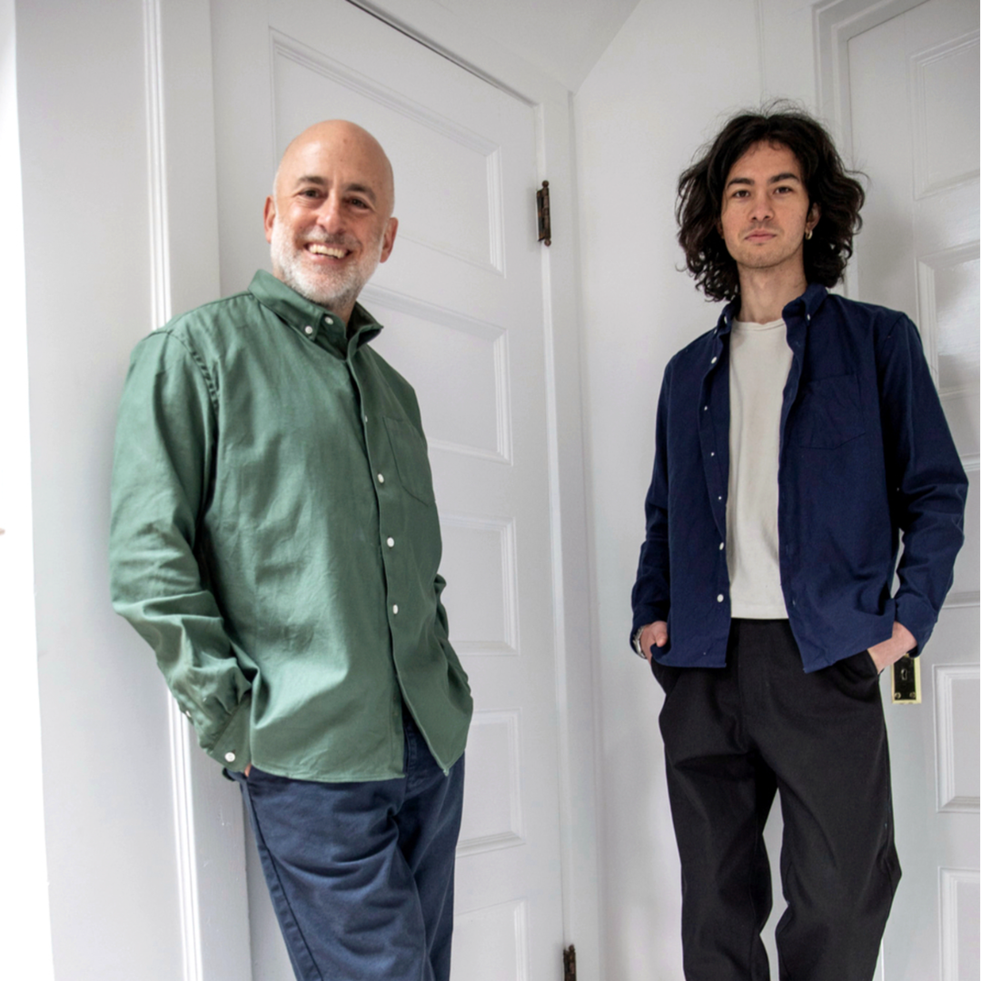 Two men, Steven Alan and his son, standing in a room with white walls and a door.